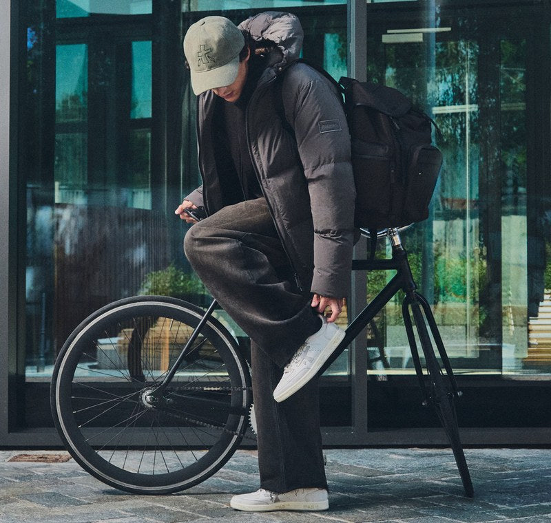 Mann auf dem Fahrrad mit weißen Premiata-Sneakern, daneben eine Detailaufnahme des Sneakers auf dem Pedal. Foto @premiataofficial